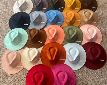 Könnte beinhalten: Eine Sammlung zahlreicher Fedora-Hüte in einer Vielzahl von Unifarben, darunter Rot, Pink, Blau, Grün, Gelb, Orange, Braun, Schwarz und Weiß. Jeder Hut hat eine eingedrückte Krone und eine breite Krempe, angeordnet in einem gitterartigen Muster.