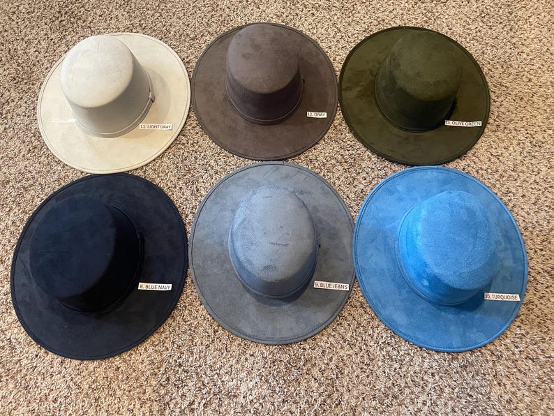 May include: Six suede-like hats in various colors are displayed. Colors include light gray, gray, olive green, navy blue, blue jeans, and turquoise. Each hat has a wide brim and a cylindrical crown. Small labels identify each color.