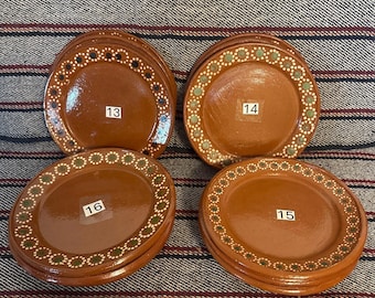 May include: Four stacks of round brown ceramic plates with glossy finishes. Each plate features a decorative border of small white and green dots. White rectangular labels with the numbers 13, 14, 15, and 16 are affixed to the center of each stack.