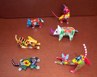 Pode incluir: Uma coleção de figuras de animais de madeira pintadas à mão. As figuras incluem um tigre, um gato, um rinoceronte e outras criaturas, cada uma com padrões e desenhos únicos. Os animais são pintados com cores brilhantes e detalhes florais.