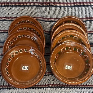 May include: Two stacks of brown clay bowls with a glossy finish, each featuring a hand-painted floral pattern in white and green along the inner rim. The front-most bowls display white square labels with the black printed numbers 43 and 44.