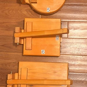 May include: Three wooden cajon drums with different shapes and sizes. The top drum is round with the number 5, the middle drum is rectangular with the number 6, and the bottom drum is rectangular with the number 7.