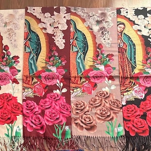 May include: Four rectangular scarves featuring a printed image of Our Lady of Guadalupe surrounded by roses. Each scarf displays a different background color: cream, maroon, taupe, and black. The scarves have fringed edges at the bottom.