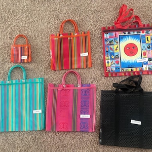 May include: A collection of six tote bags in various sizes and designs. Included are a small striped bag, a medium striped bag, a large striped bag, a pink bag with butterfly patterns, a black mesh bag, and a bag featuring a sun graphic labelled EL SOL.