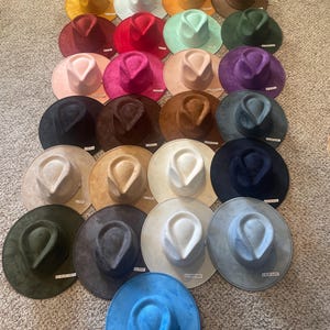 May include: A collection of twenty-five felt fedora hats arranged in a grid, featuring a wide variety of solid colours including red, yellow, white, orange, pink, green, blue, purple, brown, black, tan, and grey, each with a pinched crown.