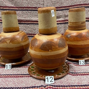 May include: Three brown ceramic pottery jars with lids, each with a different design. The jars are on a brown and white striped surface. The jars are numbered 11, 12, and 13.