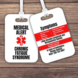 Op de afbeelding: Twee witte medische waarschuwingsbagagelabels met zwarte tekst en rode accenten. Eén label leest "MEDICAL ALERT CHRONIC FATIGUE SYNDROME" met een rood medisch symbool. De andere geeft symptomen en contactgegevens voor noodgevallen weer.