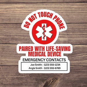 Op de afbeelding: Een witte sticker met rode accenten en tekst. De bovenkant van de sticker leest "DO NOT TOUCH PHONE" in het rood. Daaronder een rode cirkel met een wit medisch symbool. De onderkant van de sticker leest "PAIRED WITH LIFE-SAVING MEDICAL DEVICE" en "EMERGENCY CONTACTS".