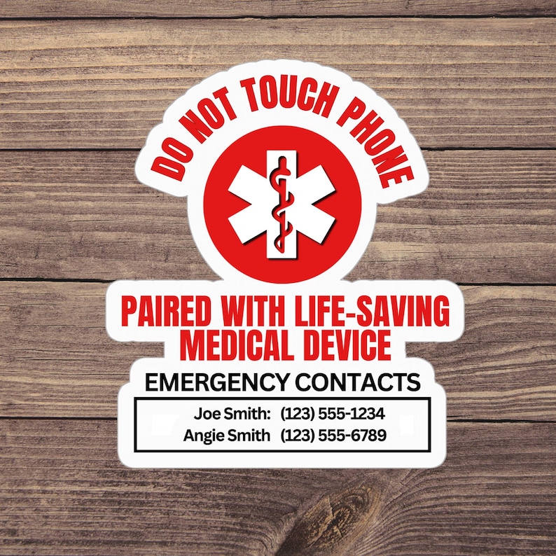 Op de afbeelding: Een witte sticker met rode accenten en tekst. De bovenkant van de sticker leest "DO NOT TOUCH PHONE" in het rood. Daaronder een rode cirkel met een wit medisch symbool. De onderkant van de sticker leest "PAIRED WITH LIFE-SAVING MEDICAL DEVICE" en "EMERGENCY CONTACTS".