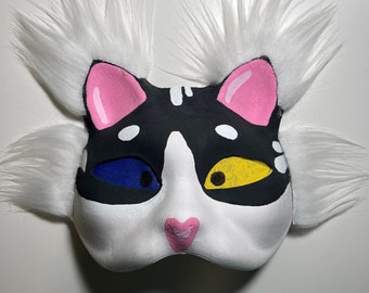 May include: A white cat mask with black and white markings, blue and yellow eyes, and pink ears and nose.