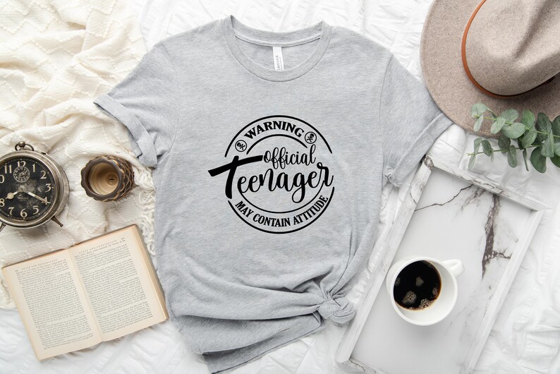 Peut inclure: T-shirt gris avec un graphique circulaire noir qui dit "Avertissement&nbsp;: Adolescent officiel Peut contenir de l'attitude".