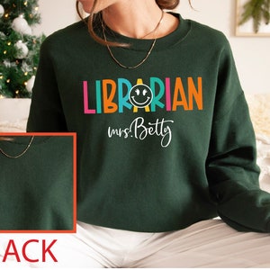 May include: Green sweatshirt with the text "LIBRARIAN mrs. Betty" in colorful letters with a smiley face in the middle of the word "LIBRARIAN".