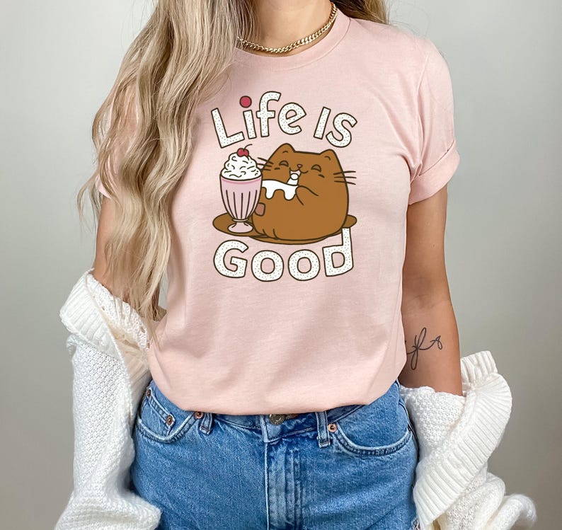 May include: A pink t-shirt with a cartoon cat drinking a milkshake. The text "Life is Good" is printed on the shirt.
