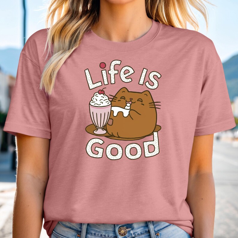 May include: A pink t-shirt with a cartoon cat enjoying a milkshake. The text "Life is Good" is printed on the shirt.