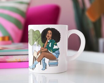 May include: White ceramic mug featuring an illustration of a woman with dark curly hair, wearing a green and white sweater, denim shorts, and blue boots. She is sitting on a stack of books, holding a book, with a plant in the background.