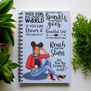 May include: A blue spiral notebook with an illustration of a young woman wearing a red jacket, blue jeans, and headphones. The notebook features inspirational quotes, including "This girl will change the world", "She leaves a little sparkle everywhere she goes", "If you can dream it you can do it", "Beautiful girl you can do amazing things", "Reach for the stars", and "Kid you are gonna be great!"