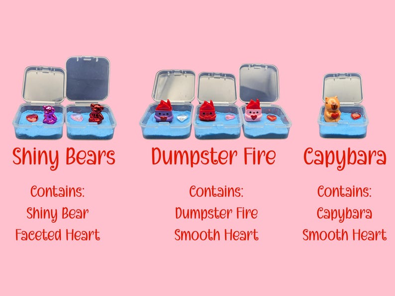 May include: Three small, open plastic containers with blue sand and miniature figurines. The containers are labeled "Shiny Bears," "Dumpster Fire," and "Capybara." Each contains a small figurine and a heart. The background is a light pink.