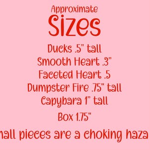 May include: A pink background with red text that reads "Approximate Sizes." Below, it lists the sizes of various items: Ducks .5" tall, Smooth Heart .3", Faceted Heart .5, Dumpster Fire .75" tall, Capybara 1" tall, and Box 1.75".