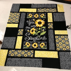 Può includere: Trapunta nera e gialla con un motivo a girasole e il testo "You are my Sunshine".