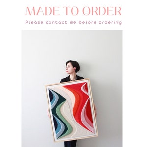 Può includere: Una donna tiene in mano un'opera d'arte astratta incorniciata con forme colorate, testurizzate e sovrapposte in tonalità di rosso, rosa, blu, verde e bianco. L'opera è incorniciata in una cornice di legno naturale.