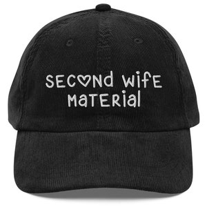 May include: Black corduroy baseball cap with white embroidered text that reads "Second wife material" with a heart symbol.