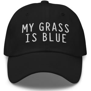 May include: Black baseball cap featuring the embroidered text "MY GRASS IS BLUE" in white. The cap has a curved peak and a structured design. A classic, casual accessory.