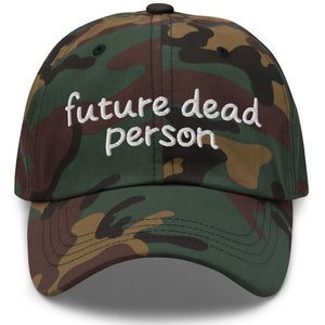 Könnte beinhalten: Eine Baseballkappe in Tarnmuster mit dem in Weiß gestickten Text "future dead person" auf der Vorderseite.