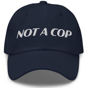May include: A navy blue baseball cap with white embroidered text that reads "NOT A COP".