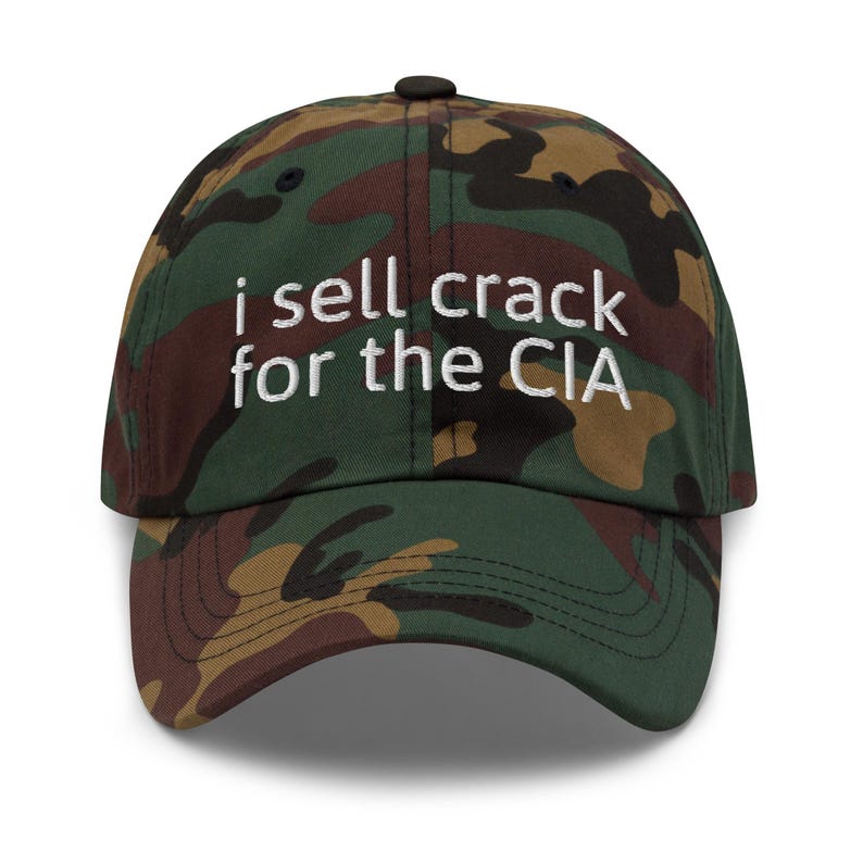 May include: A camouflage baseball cap with the text "i sell crack for the CIA" embroidered in white.