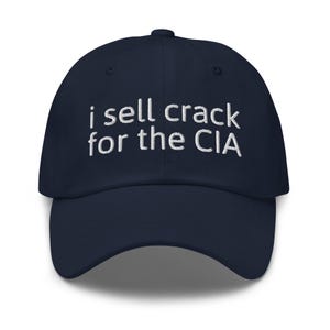 May include: A navy blue baseball cap with white embroidered text that reads "i sell crack for the CIA".