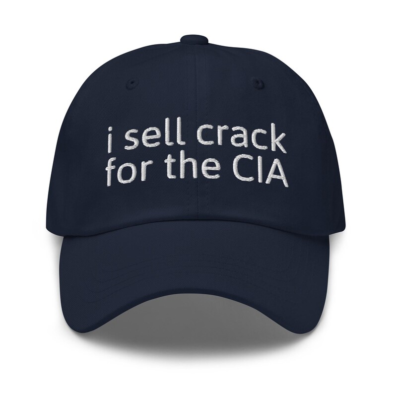 May include: A navy blue baseball cap with white embroidered text that reads "i sell crack for the CIA".