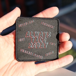 May include: Black square patch with white text that reads "ALWAYS TACO 2SDAY" in a 3D style. The text is outlined in red. The patch has white text around the edges that reads "ORIGINAL", "COUSINE", "FLAVOURS", "FAMILY", "BUILT", "130Y", "1957".