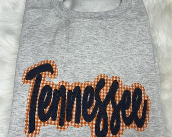 May include: Gray sweatshirt with a black and orange checkered "Tennessee" design.