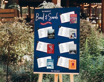 May include: A blue chalkboard sign with white text announcing the wedding of Brad and Sarah on Friday, July 8th, 2022. The sign is decorated with book covers and numbers for a seating chart.