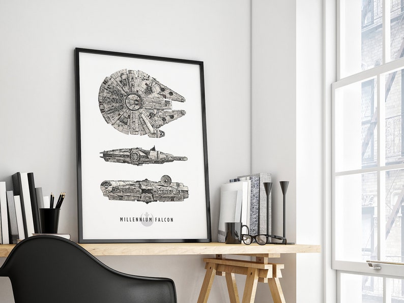May include: A black and white line drawing of the Millennium Falcon spaceship in three different views. The drawing is framed in a black frame and hanging on a white wall.