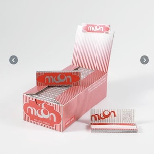 May include: A display box of "Moon" brand rolling papers. The box is red with vertical white stripes and the brand name in a white, stylized font. A smaller pack of papers and a single paper are also visible.