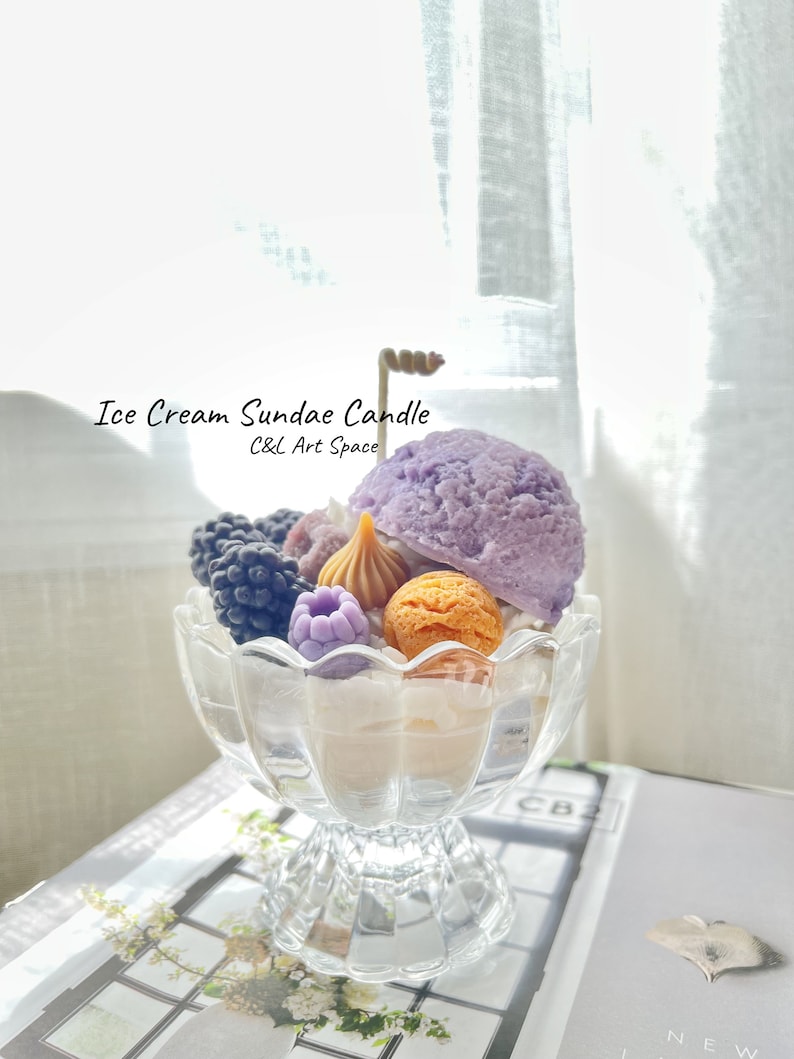 May include: A purple, white, and brown ice cream sundae candle in a clear glass dish. The candle is decorated with blackberries, raspberries, and a caramel swirl. The text "Ice Cream Sundae Candle" and "C&L Art Space" is visible on the image.
