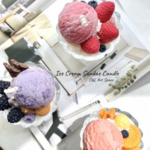 May include: Three ice cream sundae candles in clear glass dishes. The candles are decorated with various toppings, including strawberries, blueberries, chocolate, and orange slices. The candles are labeled "Ice Cream Sundae Candle" and "C&L Art Space".