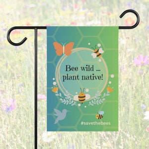 Könnte beinhalten: Eine grüne Gartenflagge mit einem Wabenmuster und einem Kreis mit dem Text "Bee wild... plant native!" und dem Hashtag "#savethebees". Die Flagge zeigt einen Schmetterling, einen Kolibri und drei Bienen.
