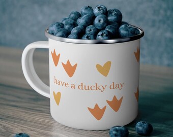 May include: White enamel mug with a duck footprint design and the text "have a ducky day". The mug is filled with blueberries.