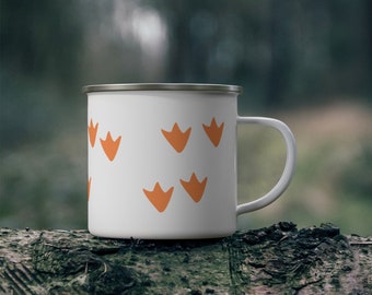 May include: White enamel camping mug with orange duck footprints printed on the side. The mug is sitting on a tree trunk.
