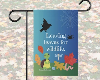 Puede incluir: Una bandera de jardín azul con una telaraña blanca y una araña colgando de ella. El texto en la bandera dice "Leaving leaves for wildlife." También hay ilustraciones de un pájaro, una tortuga, una libélula, un gusano y hojas. El hashtag #leavetheleaves está en la parte inferior de la bandera.