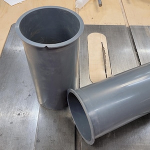May include: Two gray plastic tubes, one standing upright and the other lying on its side, on a metal surface. The tubes are likely for a woodworking project.