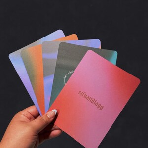 May include: A hand holds a fanned deck of cards with a gradient color scheme. The cards display hues of blue, orange, green, and pink. The text "sifuanàdlagg" is printed on the pink card.