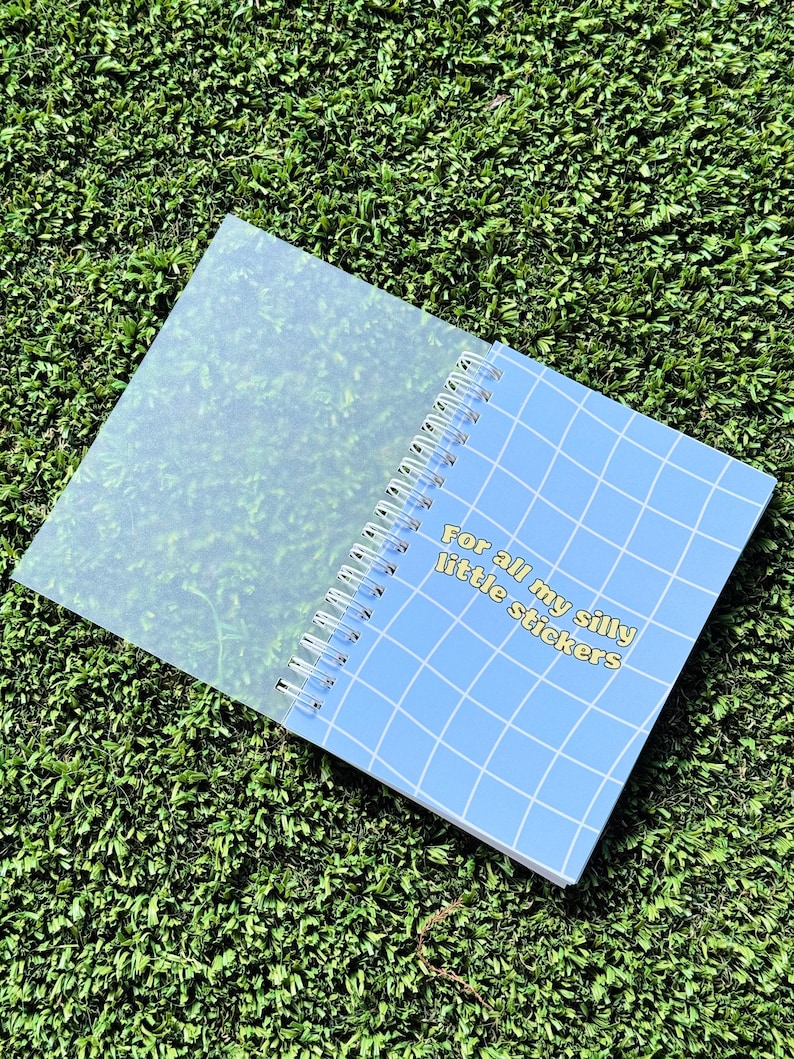 May include: A blue spiral bound notebook with a grid pattern and the text "For all my silly little stickers" in yellow. The notebook has a clear plastic cover.