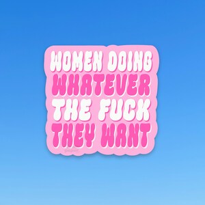May include: A pink sticker with the text "WOMEN DOING WHATEVER THE FUCK THEY WANT" in white and pink bubble letters. The sticker has a rounded rectangular shape and is set against a blue background.