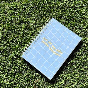 May include: A blue spiral bound notebook with a grid pattern and the text "For all my silly little stickers" in yellow.