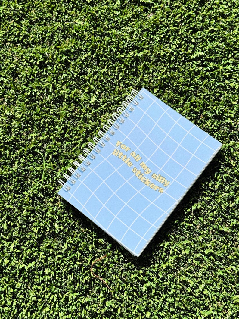 May include: A blue spiral bound notebook with a grid pattern and the text "For all my silly little stickers" in yellow.