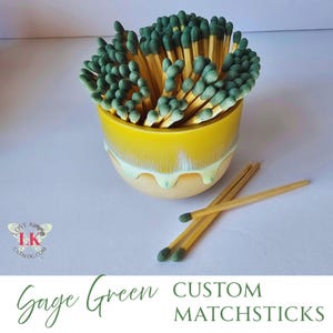 May include: A yellow ceramic bowl filled with green and yellow matchsticks. The bowl has a white glaze that drips down the sides.  There are three green and yellow matchsticks on a white surface next to the bowl.