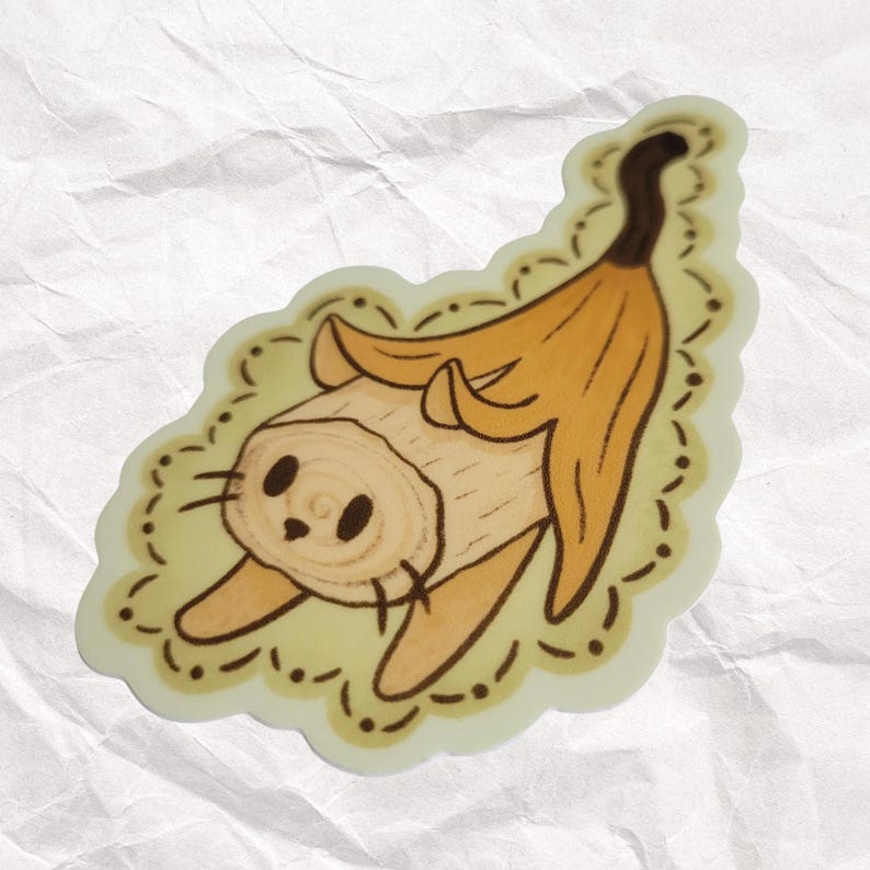 Puede incluir: Una pegatina de un gato de dibujos animados hecho de una c&aacute;scara de pl&aacute;tano. El gato tiene un cuerpo marr&oacute;n y una c&aacute;scara de pl&aacute;tano amarilla para la cabeza. El gato est&aacute; sentado sobre un fondo amarillo con un borde marr&oacute;n.